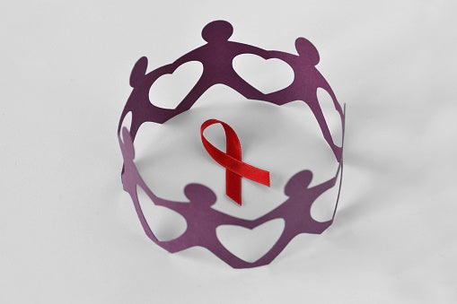 Paper people in a circle around red ribbon on white background - Aids awareness concept